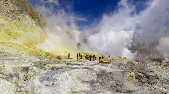 Gruppe von Menschen vor weiß dampfenden Fumarolen und Lavasee