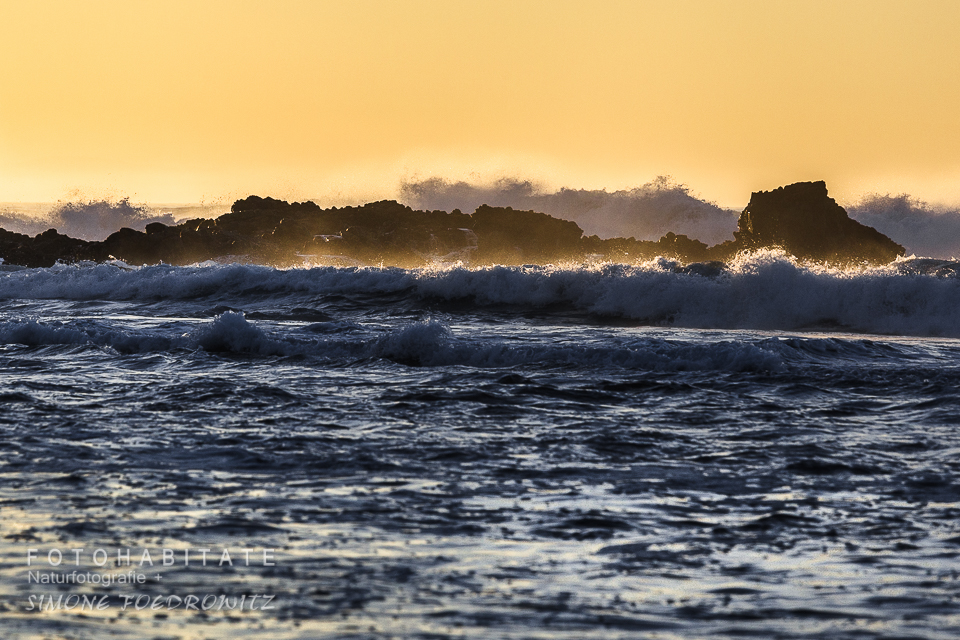 weiße Schaumkronen von Wellen vor orangem Himmel