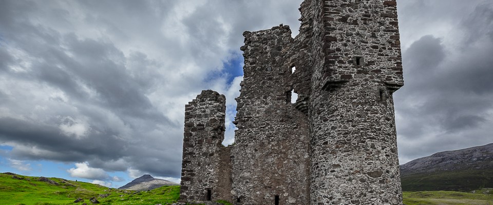 Burgruine auf grüner Wiese unter dicken Wolken