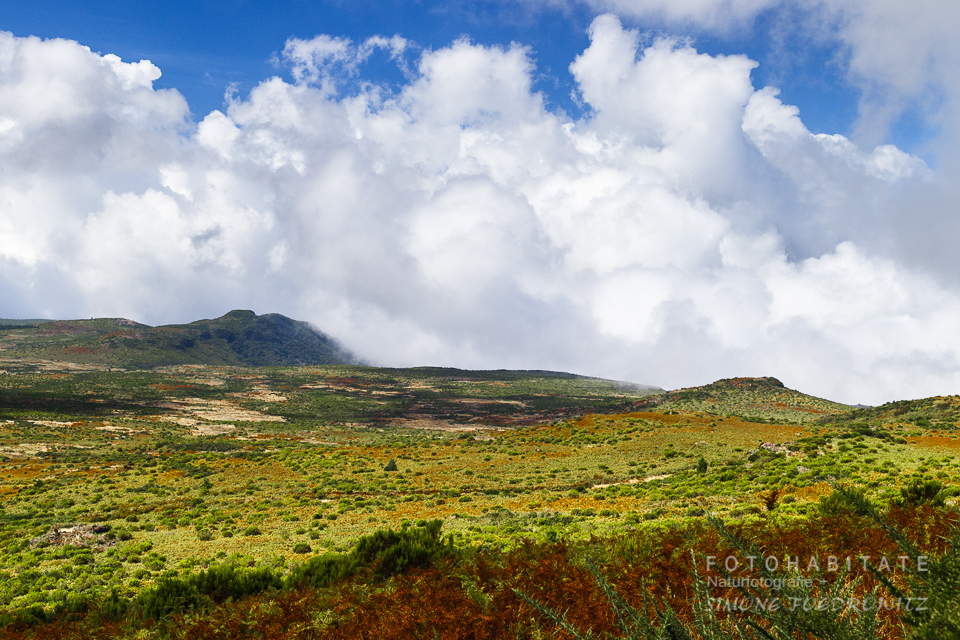 Wolken über grüner und oranger Hochlandschaft