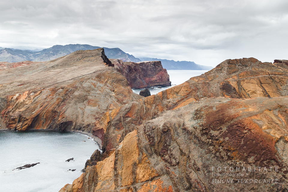 Orangebraune Felsinsel unter grauem Himmel