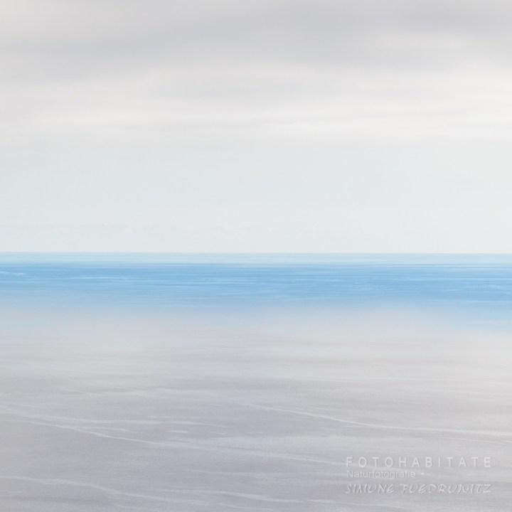 Blauer Meeresstreifen zwischen grauen Wolken und grauem Wasser