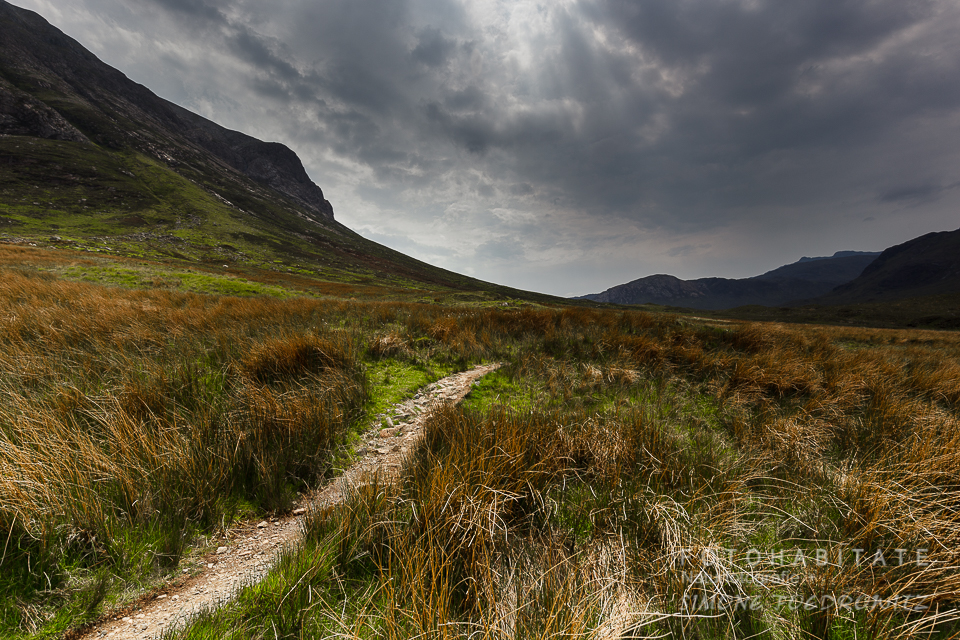 Pfad zwischen Bergen unter dunklem Wolkenhimmel