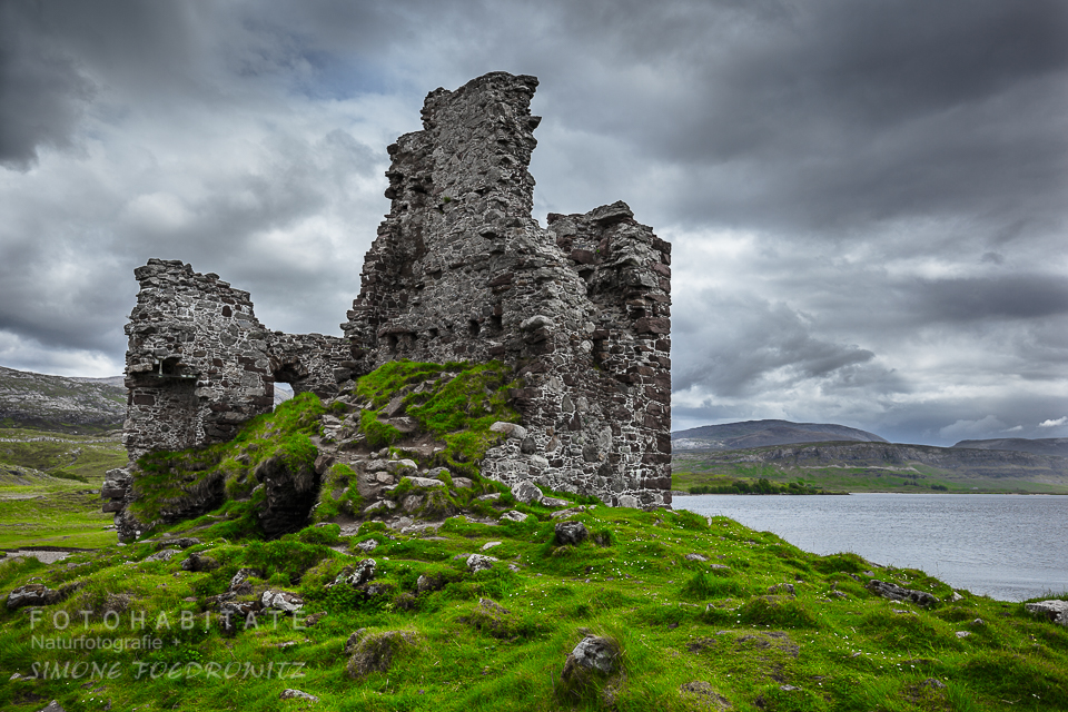 Burgruine auf grüner Wiese unter dicken Wolken