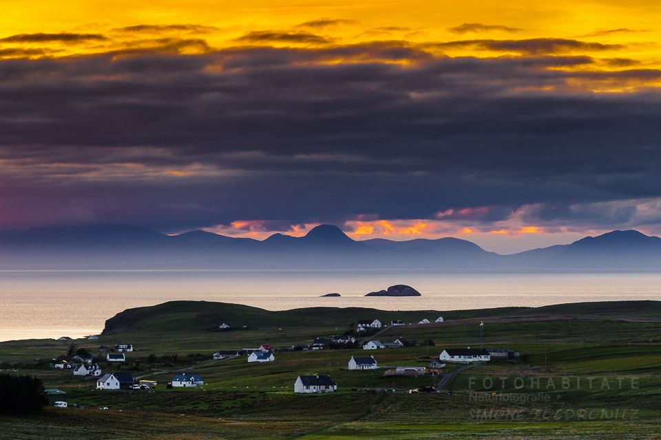 oranger Sonnenuntergang mit dunklen Wolken über Meer mit Häusern