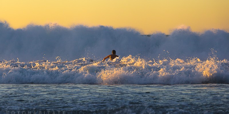 Mann in Brandung im goldenen Licht des Sonnenuntergangs