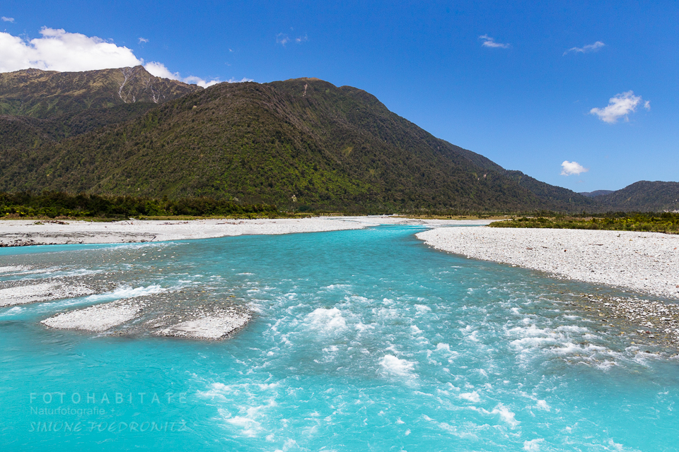 blauer Fluss in weißem Kiesbett zwischen Bergen