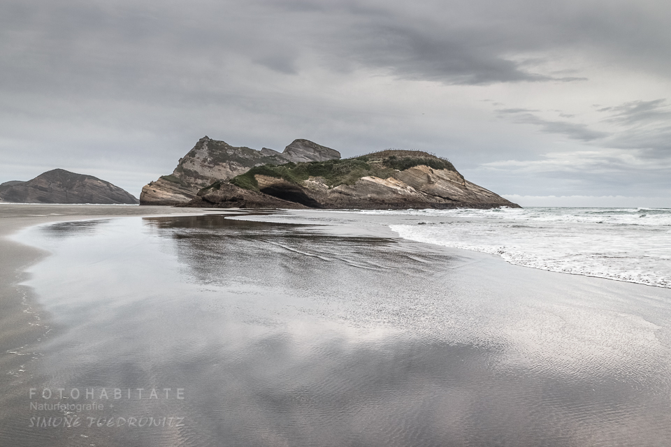 Fels spiegelt sich bei Ebbe im nassen Sandstrand