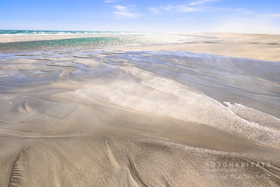 glänzender Sandstrand bei Ebbe durch abfließendes Wasser