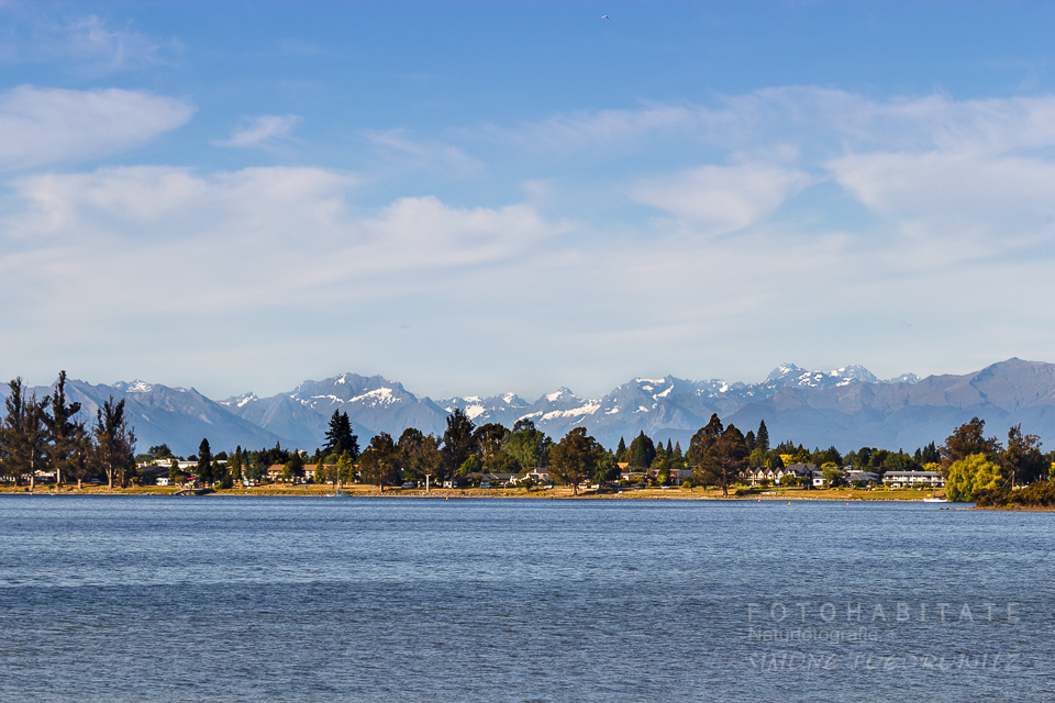 Ufer mit Häuser am See vor schneebedeckten Bergen