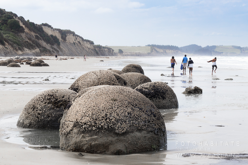 Steinkugeln am Strand mit vier Jugendlichen im Hintergrund